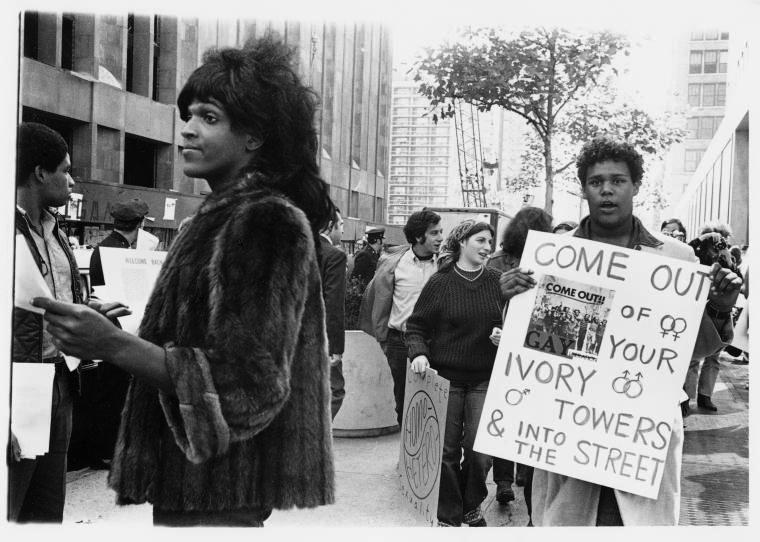 The photo depicts Marsha P. Johnson, an African-American gay liberation activist, handing out flyers in support of queer students at NYU outside of Weinstein Residence Hall in 1970.
