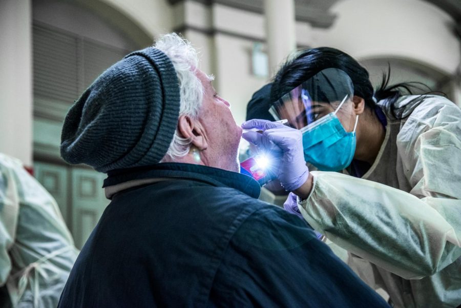 Second-year College of Dentistry student Amera Al-Faleh examines a patients teeth at an outreach event, while another student shines a phone flashlight to give a better view.