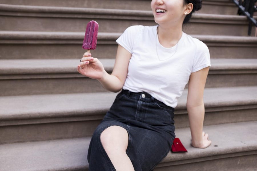 An NYU student enjoys a popsicle on the steps of an apartment building on 12th Street.