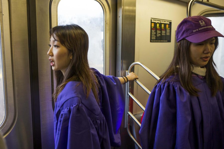 Two students in their gowns on the 4 train on their way to Yankee Stadium.