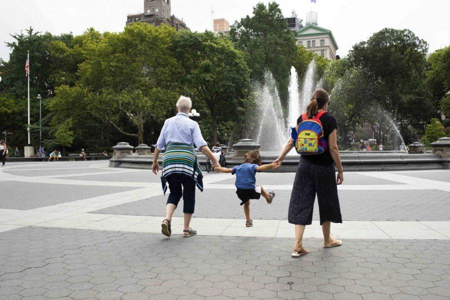 A boy jumps while holding his two guardians hands in Washington Square Park, the location .