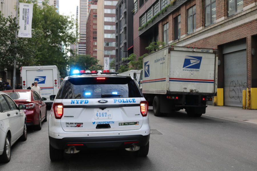 A police car weaves between US Postal Service vans nearby NYU Langones emergency care unit.