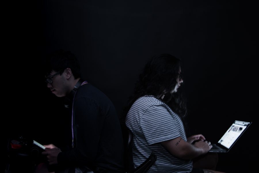 Tisch sophomore Brian Cheng (left) and Stern junior Dani Velasquez (right) sit back-to-back illuminated by phone and laptop screens, respectively. (Photo by Sam Klein)