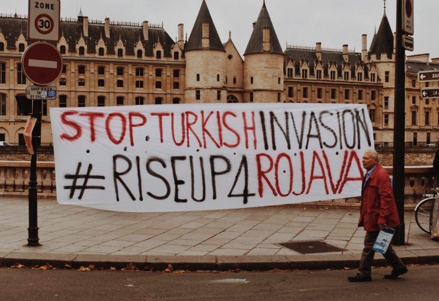 A pedestrian walking past the protest passes a banner which reads “Stop Turkish Invasion.”
