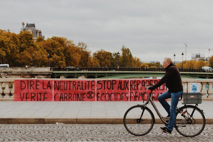 A pedestrian bikes past Extinction Rebellion sign hanging on the Seine River bridge.