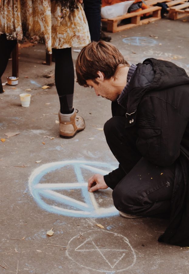 A protester draws Extinction Rebellion logo with chalk on the pavement.