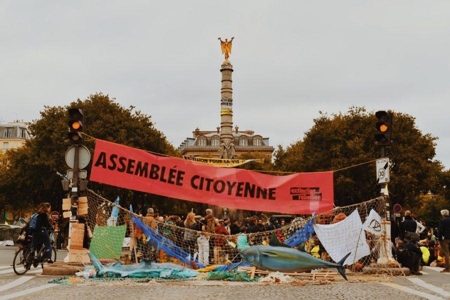 Protesters meet in front of the square with a Citizens’ Assembly banner hanging above their hands.
