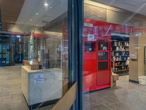The interior of an NYU academic building, with an empty public safety desk on the left, and a mailroom with a red entrance on the right.