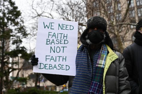 Protesters gathered in front of New York City Hall holding a sign saying "We Need Faith Based Not Faith Debased."