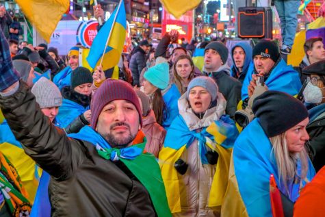 A group of protestors walking down Times Square carrying and wearing Ukrainian flags.