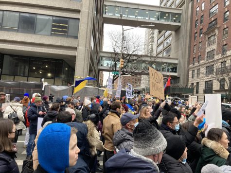 A group of protesters walking down 67th Street past the skybridge between the West and East buildings on Hunter College’s campus. The protesters carry Ukrainian flags and signs written in Ukrainian.