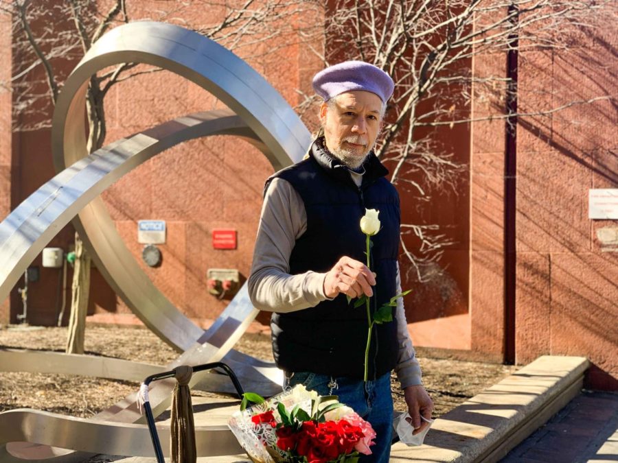Martin Fritsche stands outside Bobst Library holding a white rose.