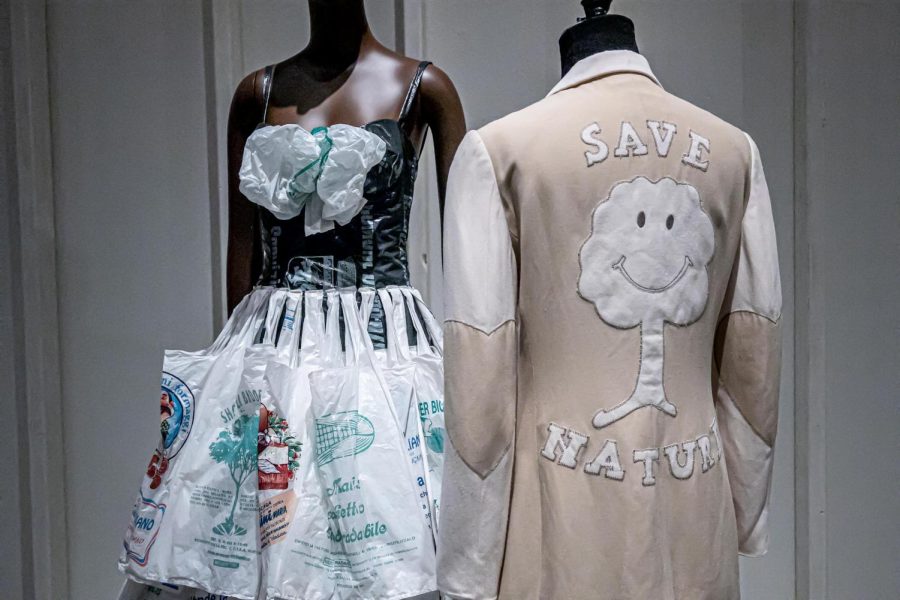 A dress made of trash bags next to brown suede coat that says “Save Nature” in the ’90s fashion exhibit at the Museum at the Fashion Institute of Technology.
