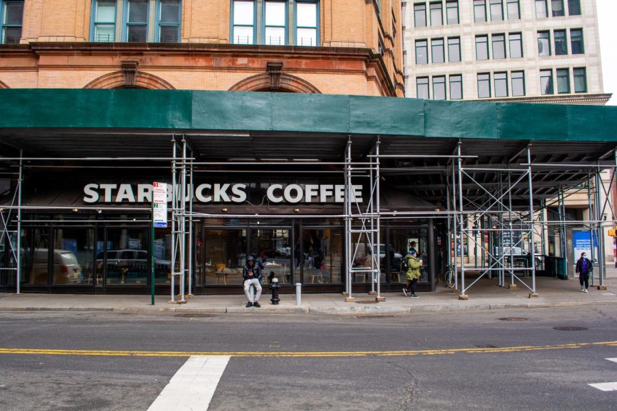 The exterior facade of the Astor Place Starbucks location is covered by scaffolding as pedestrians walk by underneath.