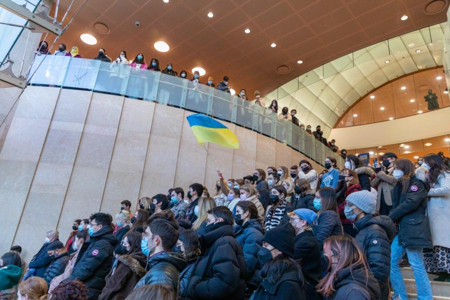 Students are seated on the lobby steps of the Kimmel Center for University Life, with one student waving a Ukrainian flag above the crowd.