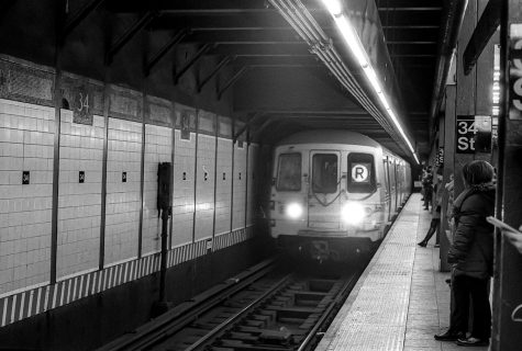 Passengers wait on the subway platform as an R train approaches the station.
