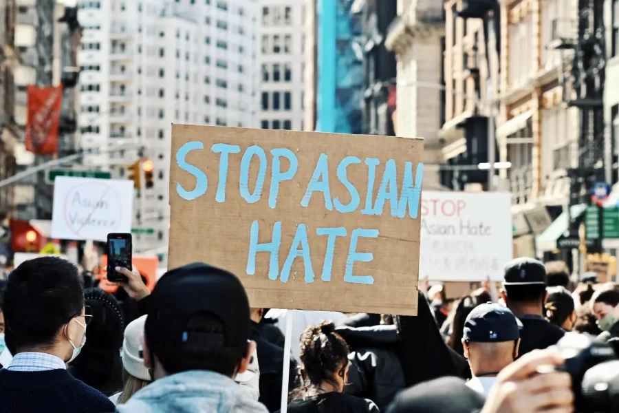 A+cardboard+sign+with+the+words+%E2%80%9CStop+Asian+Hate%E2%80%9D+in+pale+blue+letters+held+by+someone+in+a+crowd+of+protesters.