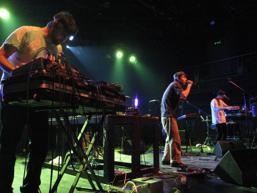 Three+members+of+Animal+Collective+performing+on+a+stage+under+green+lights.