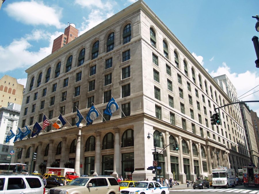 The facade of the City of New York graduate building, as seen from the corner diagonally across the street. On the left side of the building, a row of nine flags hangs above the entrance.