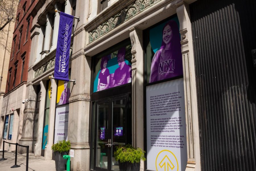 The entrance to the Bonomi Family Admissions Center. On the left, a purple banner with the building's name hangs from the side of the building. Above the entrance are posters promoting the university featuring students and alums.