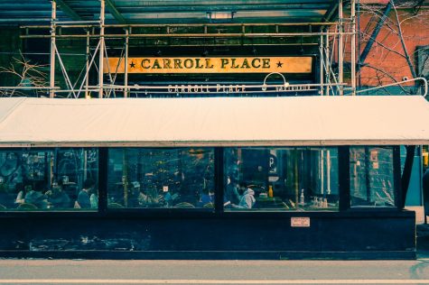 The facade and outdoor dining space of Carroll Place. Above the restaurant’s entrance is a sign with the restaurant’s name in gold letters.