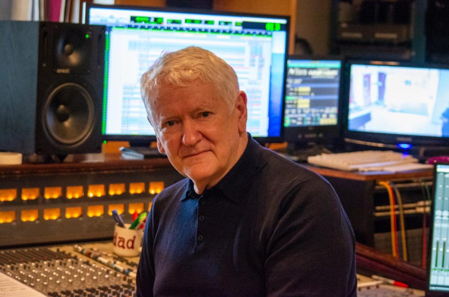 A portrait of Jim Anderson in front of a soundboard in a recording studio. He is wearing a black long-sleeve shirt.