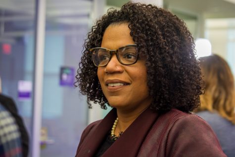 A candid portrait of Dr. Debra Furr-Holden. She is wearing a burgundy snakeskin blazer and black glasses. She is turned in profile and looks toward the left side of the frame.