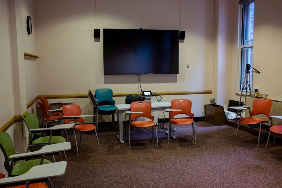 The+picture+shows+a+typical+small+NYU+classroom+with+20+tablet-arm+chairs+in+green+and+orange.+A+large-screen+TV+is+mounted+in+the+room.