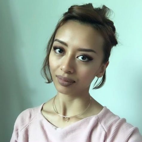 A portrait of Fiqah Rahman against a teal background. She’s wearing a blush pink shirt with her hair in an updo.