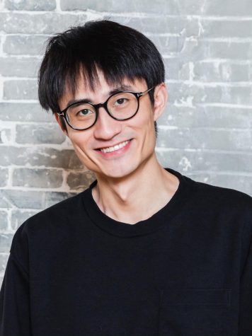 A portrait of Bohao Liu against a gray brick wall. He’s wearing a black long sleeve t-shirt and black rounded glasses.