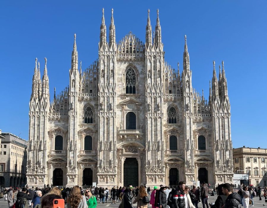 The facade of Duomo di Milano. Crowds of people are walking in front of the cathedral.