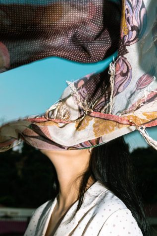 A collage of layered photographs. One image features the neck and torso of a woman. Another features a teal blue sky, and the last features multicolored textiles.