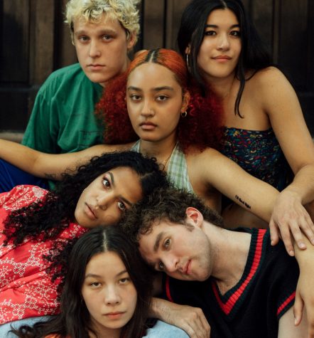 A group portrait of six singers from the music collective MICHELLE. Their heads are zippered on top of one another and all of the members are positioned in front of a brown background.