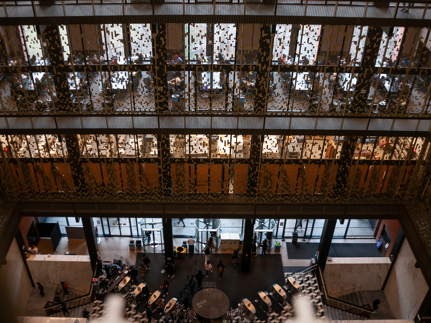 An image of Bobst Library looking down on the ground-floor atrium. On each level, metal screens run from the floor to the ceiling.