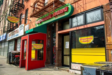 The exterior façade of a brown building with the green, red and yellow colors on the empanada mama logo on their storefront.