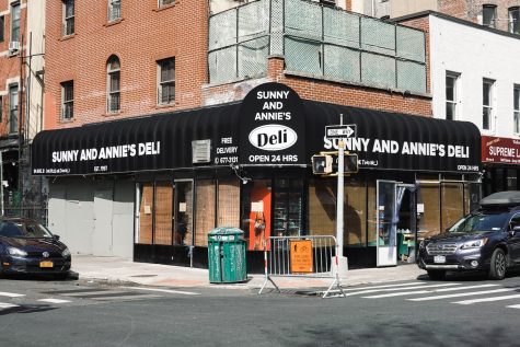 The exterior facade of a brown building with black and white signage on top of the windows of Sunny and Annie's Deli on the corner of a street.