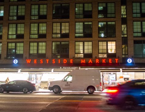 The exterior façade of an apartment building on top of the Westside Market storefront while cars park in front on Third Avenue.