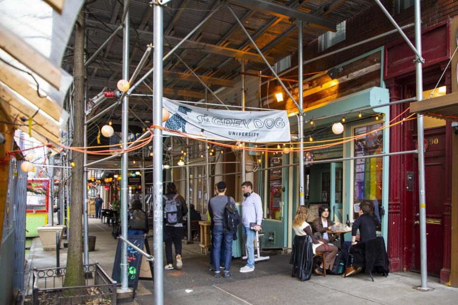 A group of people crowd around the entrance of The Grey Dog. Above them is metal scaffolding with a baby blue banner that has the restaurant’s name printed on it.