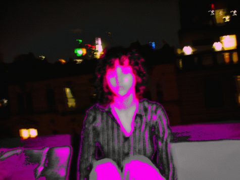 A curly-haired man sitting on a rooftop with pink around the edges of his body.