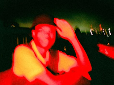 A red man with a bucket hat and yellow shirt, green blurry sky behind.