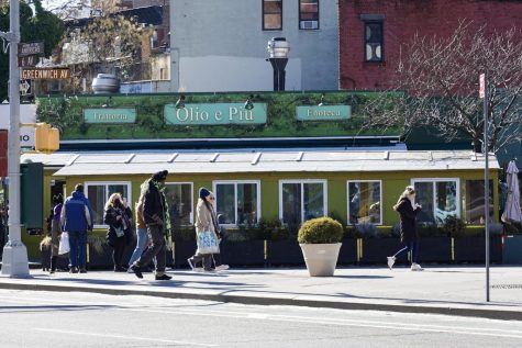 The facade of Olio e Piú seen from across Sixth Ave. Above the entrance are the words “Trattoria,” “Olio E Piú” and “Enoteca” surrounded by green vines. People walk on the sidewalk past the restaurant.