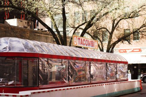 The outdoor seating structure at Tacombi, a Mexican restaurant in Greenwich Village. The name of the restaurant can be seen on a white sign above the structure. Behind the seating structure are white apple blossom trees in full bloom.