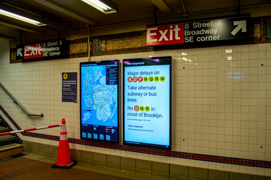 The platform of the uptown local track of the R/W trains at Eighth Street station near NYU. A screen at the platform indicates major delays of the B/D/F and N/Q/R/W lines.