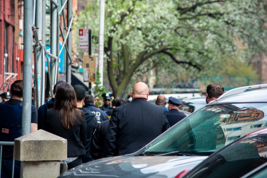 A crowd of police officers, legal personnel, reporters and civilians dressed in dark blue congregating on a sidewalk in the East Village.
