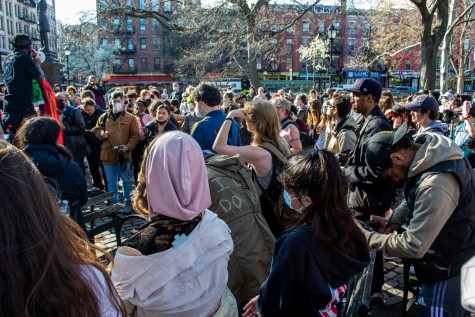 A crowd of people are gathered at a park listening to a protester speaking into a megaphone.