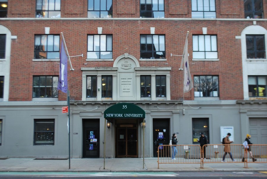 The frontal exterior of Rubin Hall. It is a brick building; the ground-floor exterior is painted gray. A green awning above door reads “35” and “New York University.” Two NYU banners flank the awning.