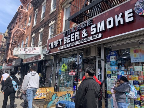 A close-up shot of the exterior of Village Craft Beer & Smoke, as well as the adjacent East Village Wines. Pedestrians walk by on the sidewalk.