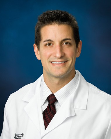 A portrait of orthopedic surgeon and sports medicine specialist Dr. Kevin Kaplan wearing a white doctor’s gown saying “Jacksonville Orthopedic Institute.”