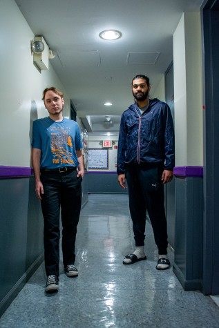 A long shot of two people standing on both sides of a hallway looking directly at the camera.
