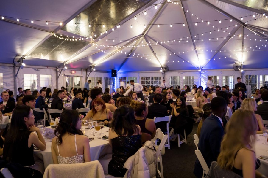 Students dressed in formal attire dining in a white tent.